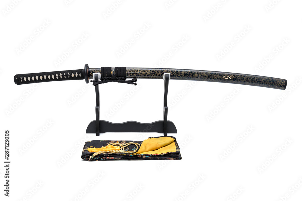 Japanese sword with textured scabbard with black cord on wooden stand  and silk  bag in front of, isolated in white background.