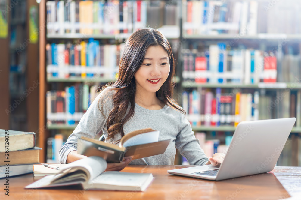 Asian young Student in casual suit doing homework and using technology laptop in library of university or colleage with various book and stationary over the book shelf background, Back to school Asian young Student in casual suit doing homework and using technology laptop in library of university or colleage with various book and stationary over the book shelf background, Back to school