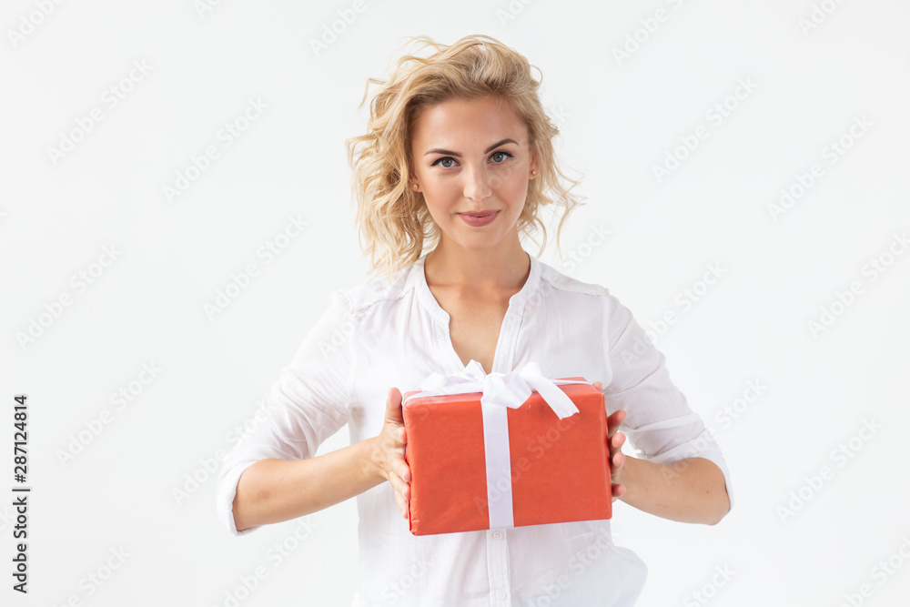 Cheerful good looking young blond woman holding a red gift box in her hands, but against a white background. Concept holidays and presents Cheerful good looking young blond woman holding a red gift box in her hands, but against a white background. Concept holidays and presents