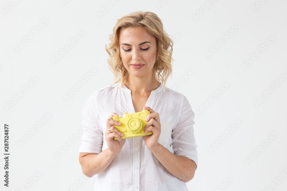 Smiling young woman is holding in her hands a yellow vintage camera model posing on a white background. Concept of amateur and professional photography. Smiling young woman is holding in her hands a yellow vintage camera model posing on a white background. Concept of amateur and professional photography.