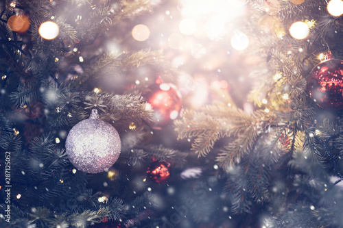 Christmas holiday background. Silver bauble hanging from a decorated on tree with bokeh and snow, copy space.