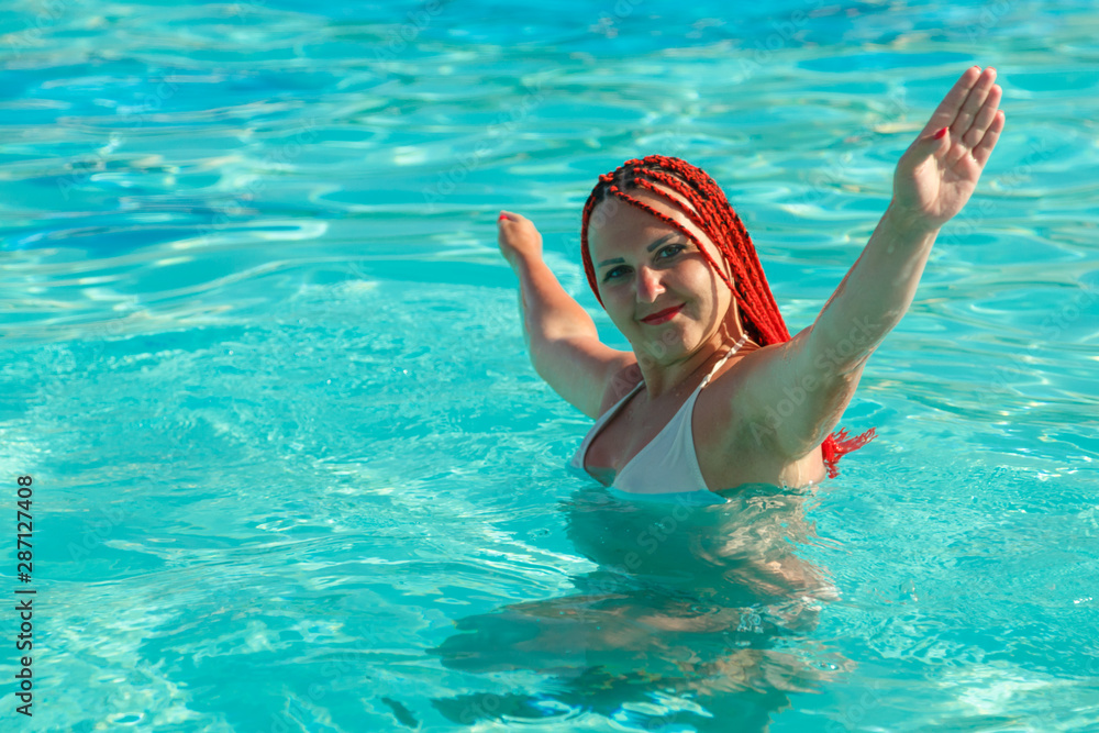 A young woman with African pigtails stands in the water in the pool.