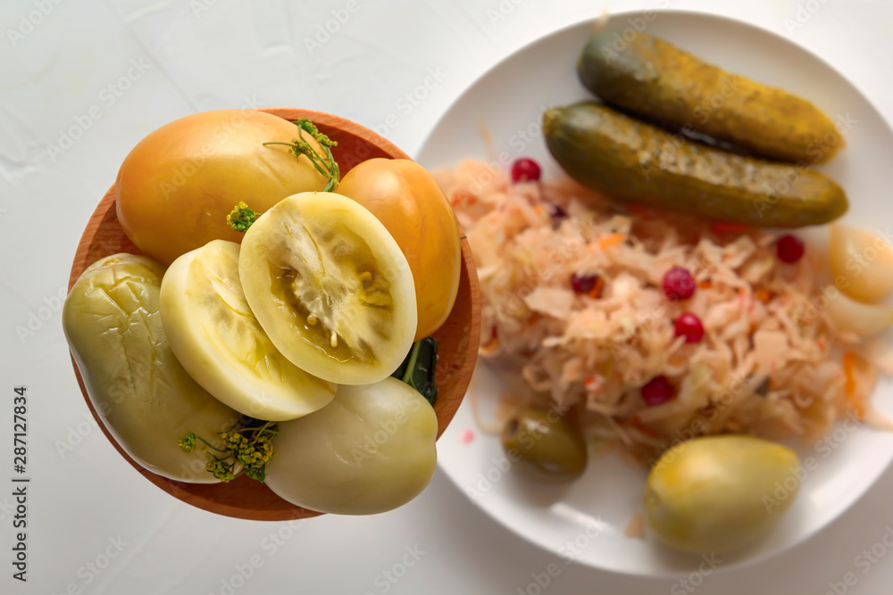 Salted tomatoes in a wooden plate on a background of fermented products on a white table. Close-up. Top view Salted tomatoes in a wooden plate on a background of fermented products on a white table. Close-up. Top view