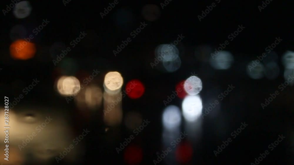 Rain water drops Falling Down On the Windscreen in slow motion, Rain Drops On The Windows Glass, Defocused Night City Traffic Lights. Color Blurred bokeh of moving transport and typical city noise. Rain water drops Falling Down On the Windscreen in slow motion, Rain Drops On The Windows Glass, Defocused Night City Traffic Lights. Color Blurred bokeh of moving transport and typical city noise.