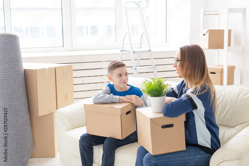 Cute single mom and little boy son sort boxes with things after the move. The concept of housewarming mortgage and the joy of new housing. Cute single mom and little boy son sort boxes with things after the move. The concept of housewarming mortgage and the joy of new housing.