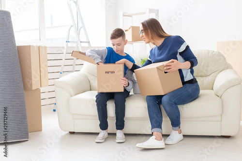 Cute single mom and little boy son sort boxes with things after the move. The concept of housewarming mortgage and the joy of new housing.