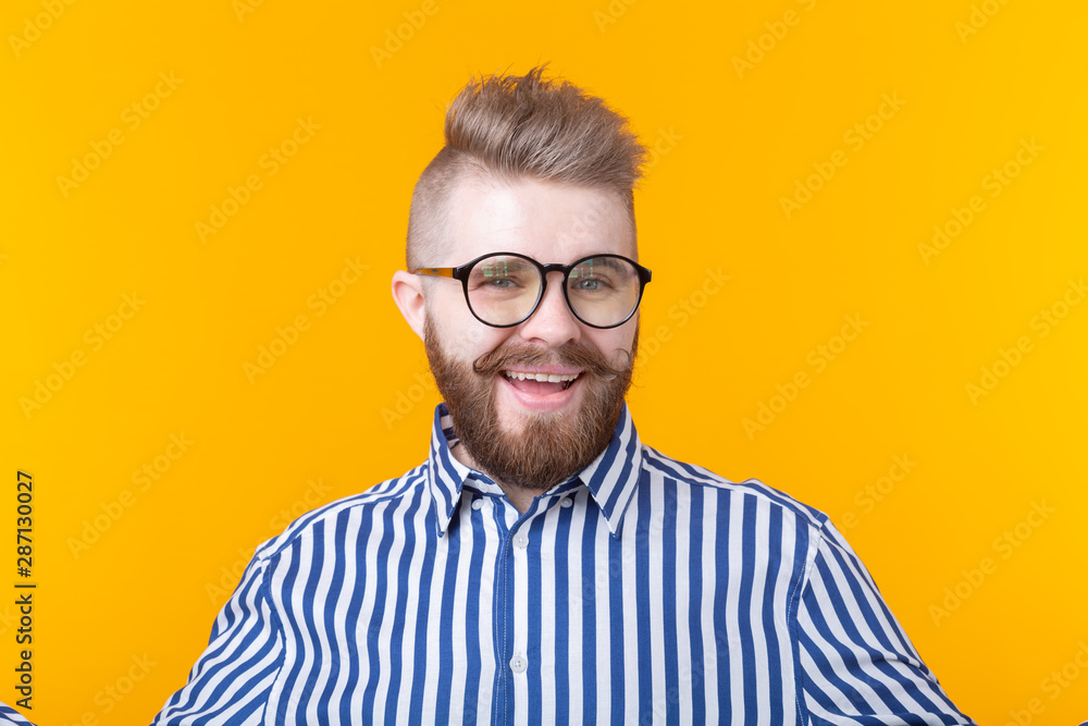 Young positive trendy man hipster with a mustache beard in shirt posing on a yellow background. Young positive trendy man hipster with a mustache beard in shirt posing on a yellow background.