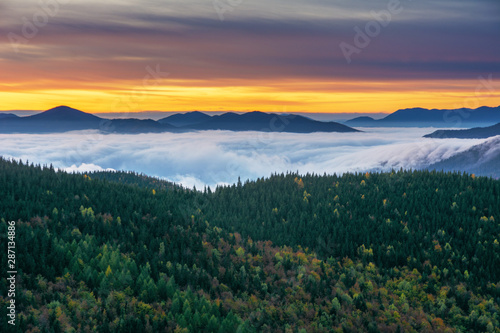 A beautiful autumn dawn in the Ukrainian Carpathian Mountains, with fogs in the valleys and forests, and yellow-red trees.