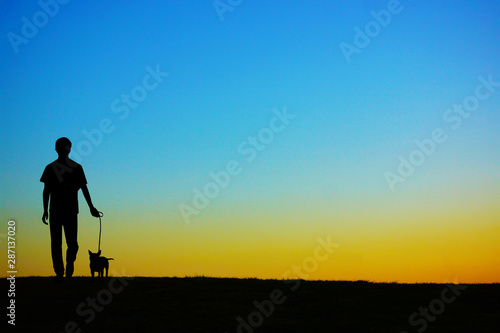 夕暮れの丘で犬の散歩をしている人