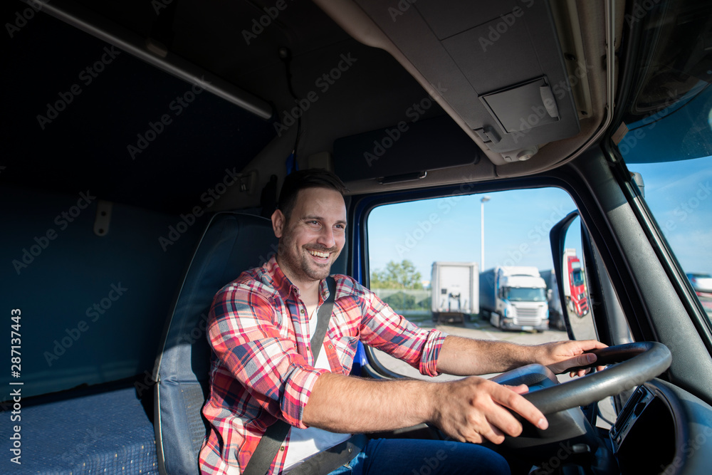 Shot of professional truck driver in casual clothing wearing seat belt on  and driving his truck to destination. Smiling trucker enjoying his job.  Transportation services. Stock-bilde | Adobe Stock
