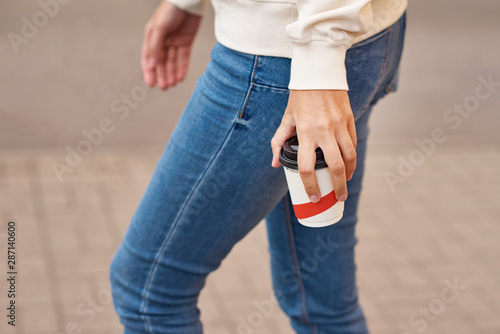 Woman hand with paper cup of coffee take away in a city street