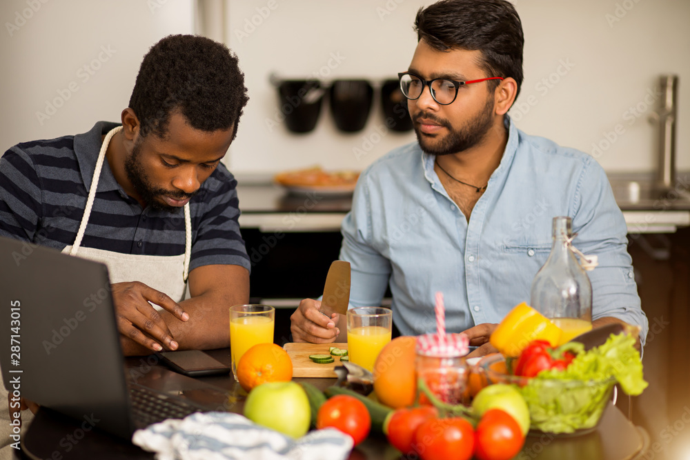 Two men using laptop in kitchen Two men using laptop in kitchen