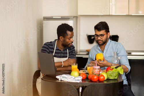 Two men using laptop in kitchen