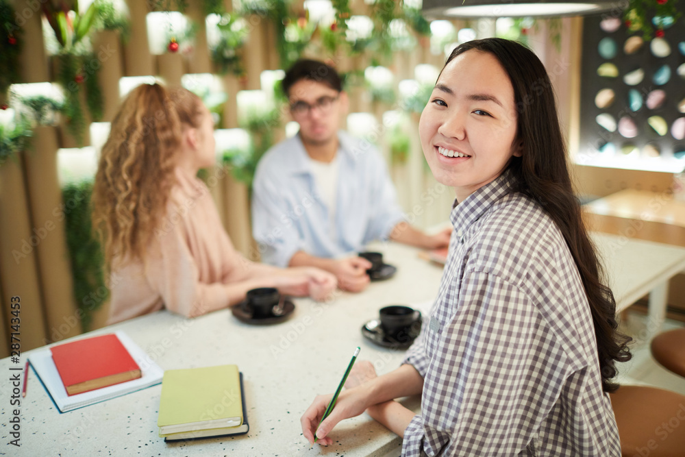 Multi-ethnic group of students studying together in cafe, focus on smiling Asian girl looking at camera, copy space Multi-ethnic group of students studying together in cafe, focus on smiling Asian girl looking at camera, copy space