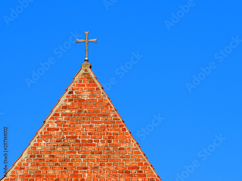 Roof of an ancient brick building with a cross on a spire against the blue sky