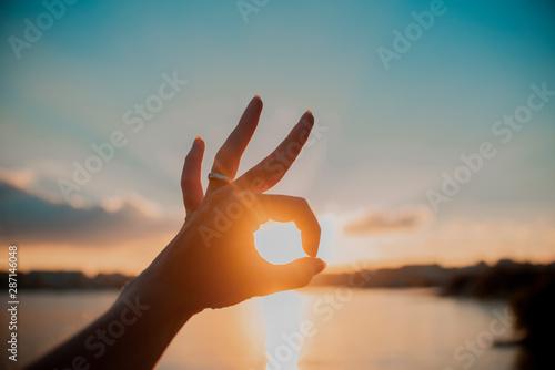 Ok hand silhouette circle the sunset with sun star at a river in the city.