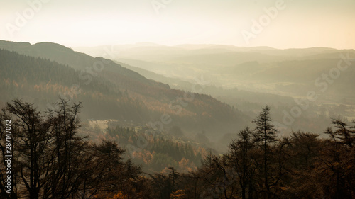 Landscape view from Gummers How in Lake District over stunning Autumn Fall color woodland with hazy unlight in late afternoon