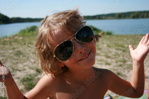 little girl sitting on the lake in sunglasses and smiling