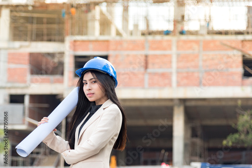 Asian woman architect wearing blue safety helmet checking working progress at construction site.