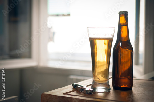 A bottle and a glass of beer and a corkscrew on wooden surface with blurred background and cinematic color grading