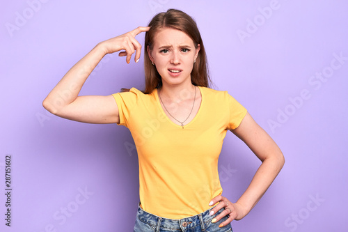 Front view of displeased clueless young woman looks with puzzlement expression  scratches head  frowning  unpleasant expression  thinks how to solve problem  feels nervous and stressed.