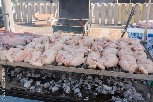 BBQ raw chicken lined up on a large outdoor grill with smoke coming up from the fire below.