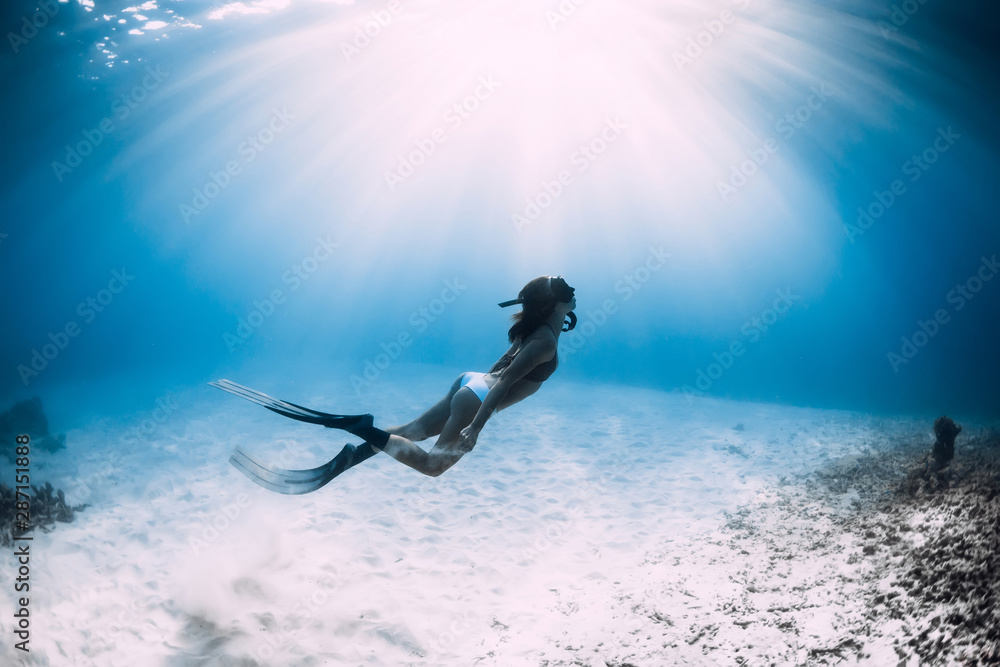 Freediver woman with fins dive over sandy sea in sea.