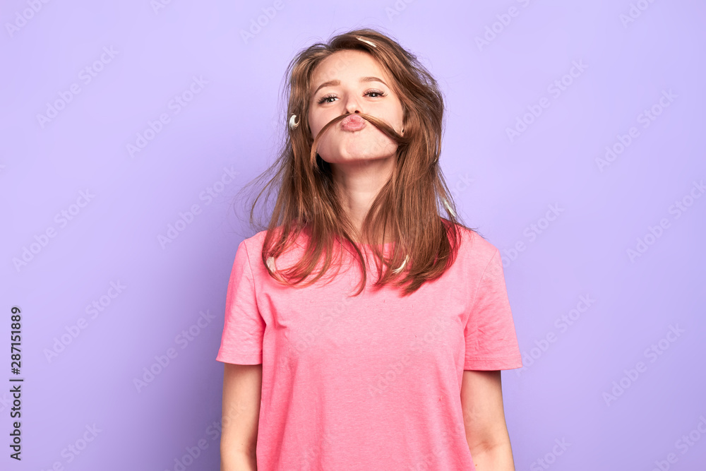 Portrait shot of cheerful funny girl having playful mood, making moustache with her hair, joking and having great time with friends at pyjamas party, lots of feathers in messy hair after pillow fight. Portrait shot of cheerful funny girl having playful mood, making moustache with her hair, joking and having great time with friends at pyjamas party, lots of feathers in messy hair after pillow fight.