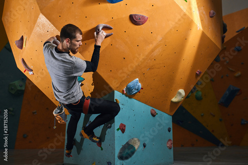 Man with physical disability rock climbing during his morning training at bouldering sport center, enjoys his extreme hobby and achieves great results. Low angle view. Active lifestyle concept.