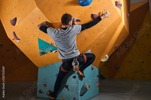 Back view of young strong sportsman without forearm rock climbing, motivated and powerful, overcomes physical disability, doesn't get discouraged, enjoys his active bouldering hobby.