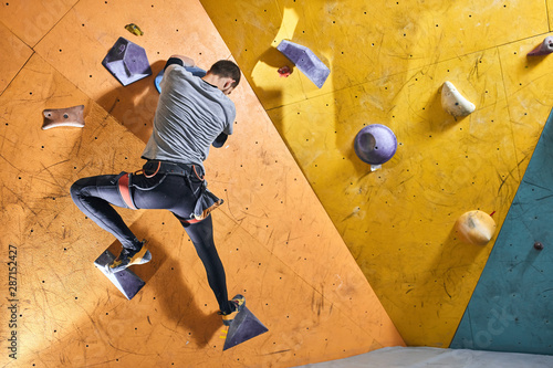 Motivation photo of powerful physically challenged boulderer climbing at artificial rock wall in indoor settings, overcomes difficultes and physical disability, positive and successful person.