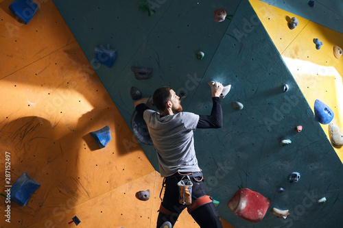 Rare view of unrecognizable male rock-climber with physical disability training at colourful artificial rock wall, hanging on two holds, has strong biceps and abs muscles, active training.