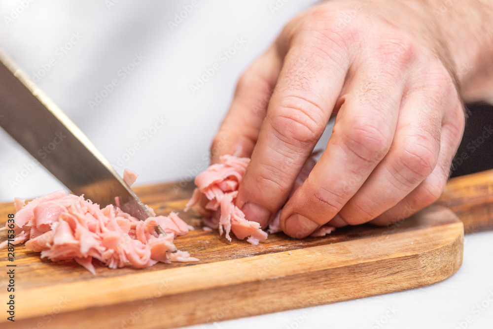 Chef slicing ham on wooden table .
