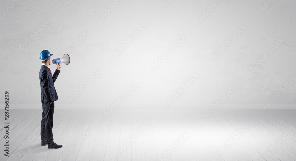 Young architect with construction helmet standing in an empty space and holding a plan Young architect with construction helmet standing in an empty space and holding a plan