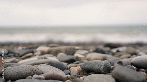 Canvas Print Pebble stones on the shore close up in the blurry light in the distance background