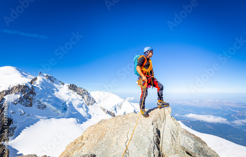 Vászonkép Alpinist mountaineer standing rock cliff mountain summit.