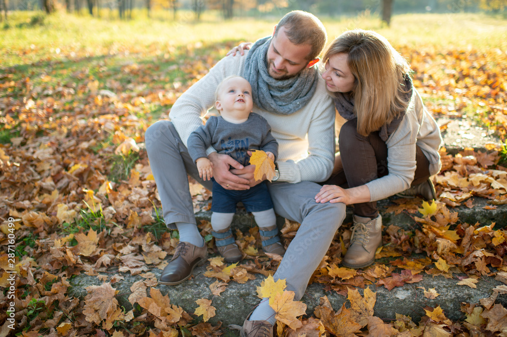 Happy family couple sitting on stairs covered by autumn leaves and holding their beautiful child.