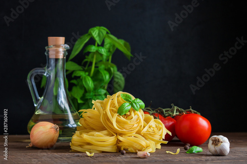raw ingredients for cooking italian pasta. fettuccine tomatoes garlic basil olive oil onion on wooden table copy space