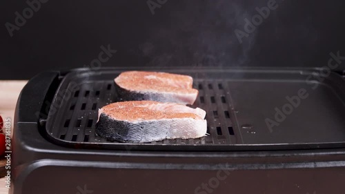 Close up of scliced fresh salmon frying on electric grill seasoned with salt and herbs. photo