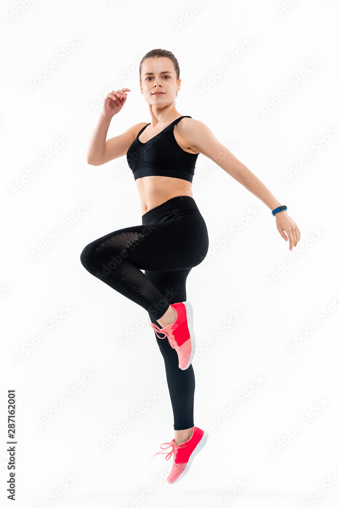 Young sporty blond woman in a black sportswear jumping isolated over white background. Sport activity
