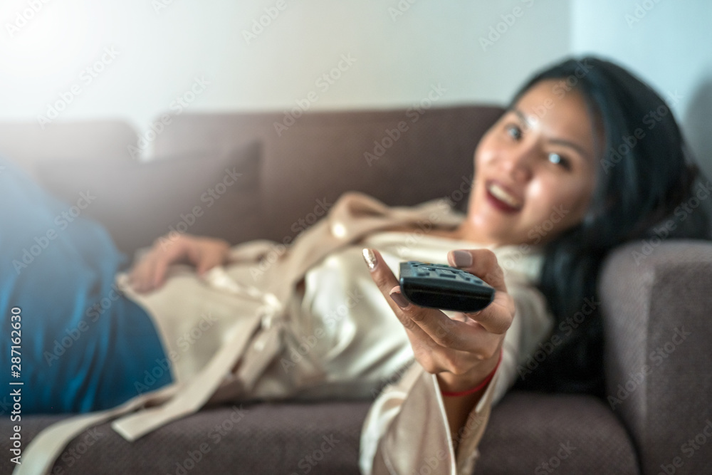 Asian woman holding a tv remote on a sofa Asian woman holding a tv remote on a sofa
