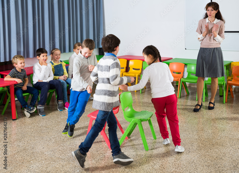 Obraz premium Kids and teacher playing musical chairs