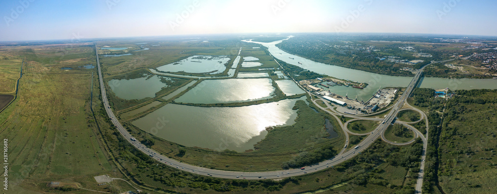Aerial view (drone view) on a sunny summer day over the Don River at the intersection with the M4-Don motorway. Road junction, bridge and port. The high right bank and the city of Aksai on its hills Aerial view (drone view) on a sunny summer day over the Don River at the intersection with the M4-Don motorway. Road junction, bridge and port. The high right bank and the city of Aksai on its hills