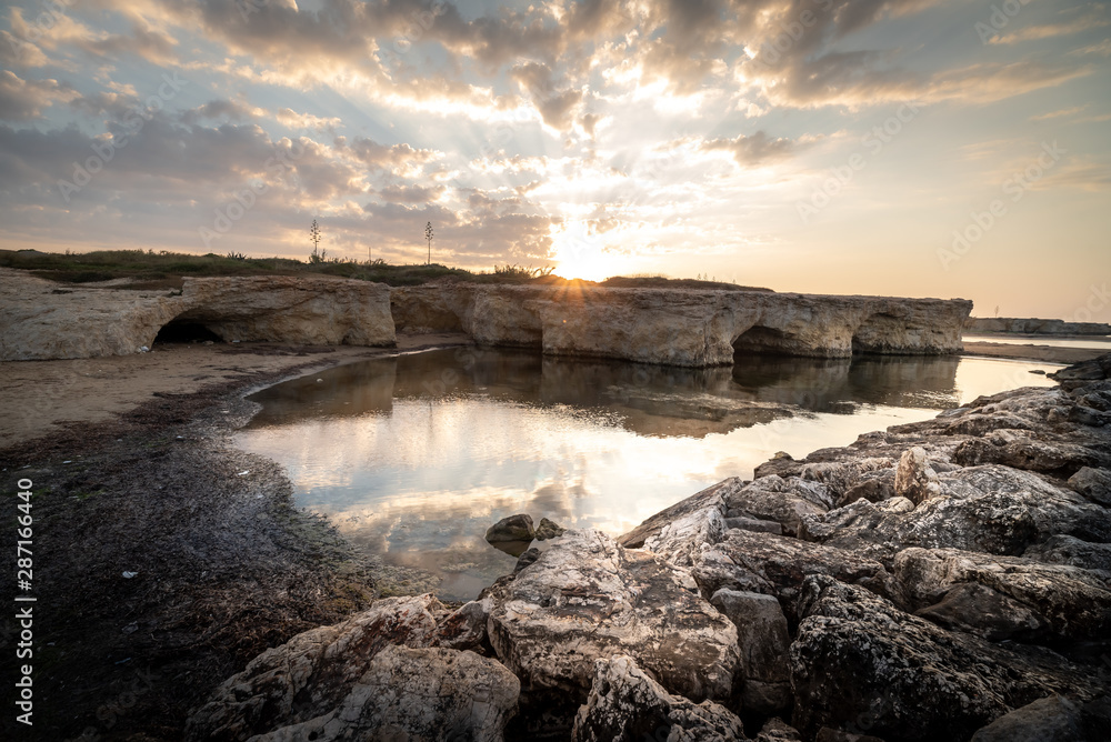 Shot of the sun rising behind the rocks at Cirica Bay at sunrise. Cirica is a beautiful nature seaside place made of cliffs, rocks and sand in the southern Sicily, Italy	