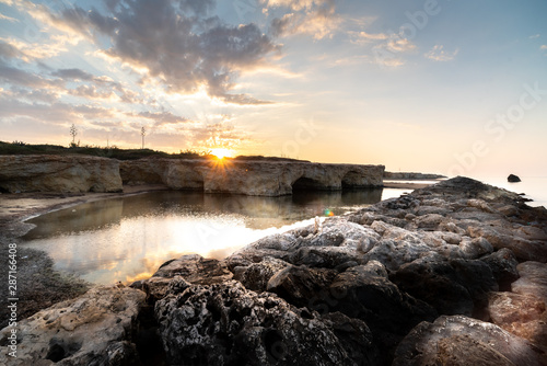 Shot of the sun rising behind the rocks at Cirica Bay at sunrise. Cirica is a beautiful nature seaside place made of cliffs, rocks and sand in the southern Sicily, Italy © gpiazzese