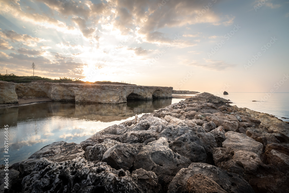Shot of the sun rising behind the rocks at Cirica Bay at sunrise. Cirica is a beautiful nature seaside place made of cliffs, rocks and sand in the southern Sicily, Italy	