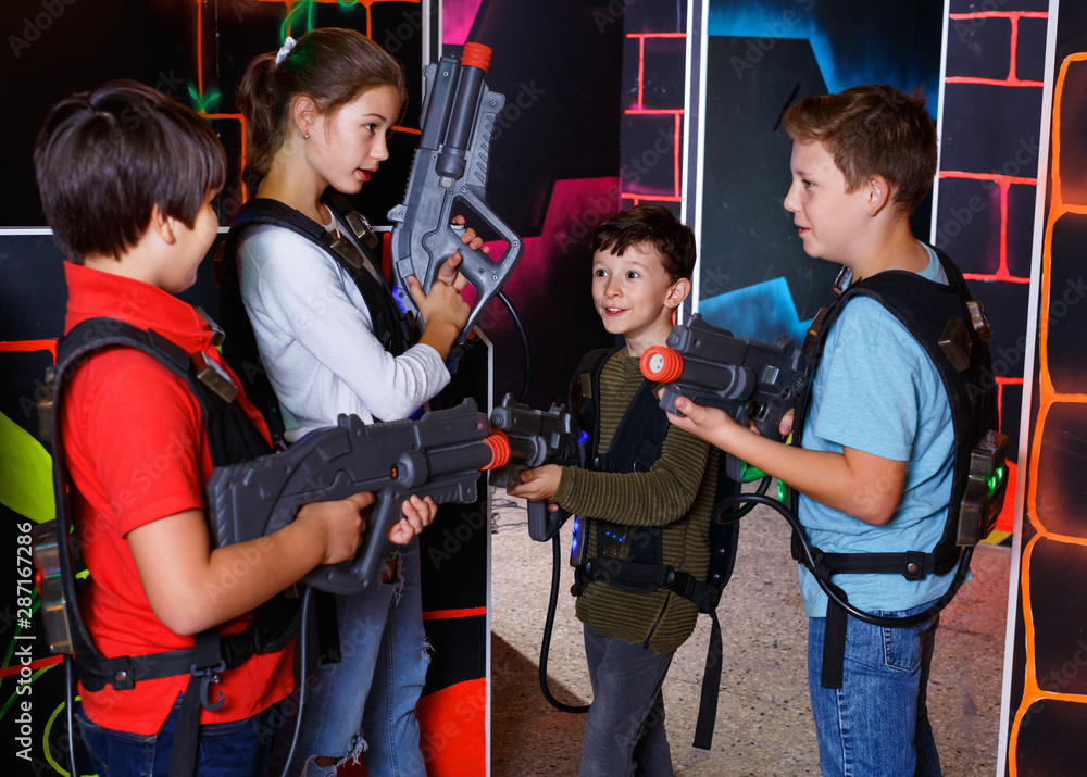 Group of happy teenagers with laser guns having fun on dark lasertag arena