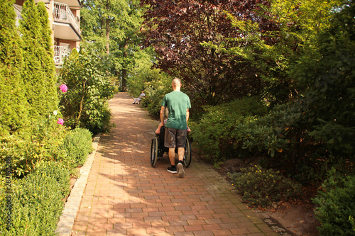 Φωτογραφία young man carries an elderly overweight woman in a wheelchair on the street