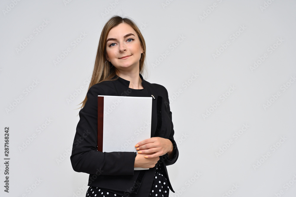 Portrait of a cute middle-aged brunette woman with beautiful curly hair and perfect face skin in a black business suit with a folder in her hands on a white background. Beauty, brightness, smile. Portrait of a cute middle-aged brunette woman with beautiful curly hair and perfect face skin in a black business suit with a folder in her hands on a white background. Beauty, brightness, smile.