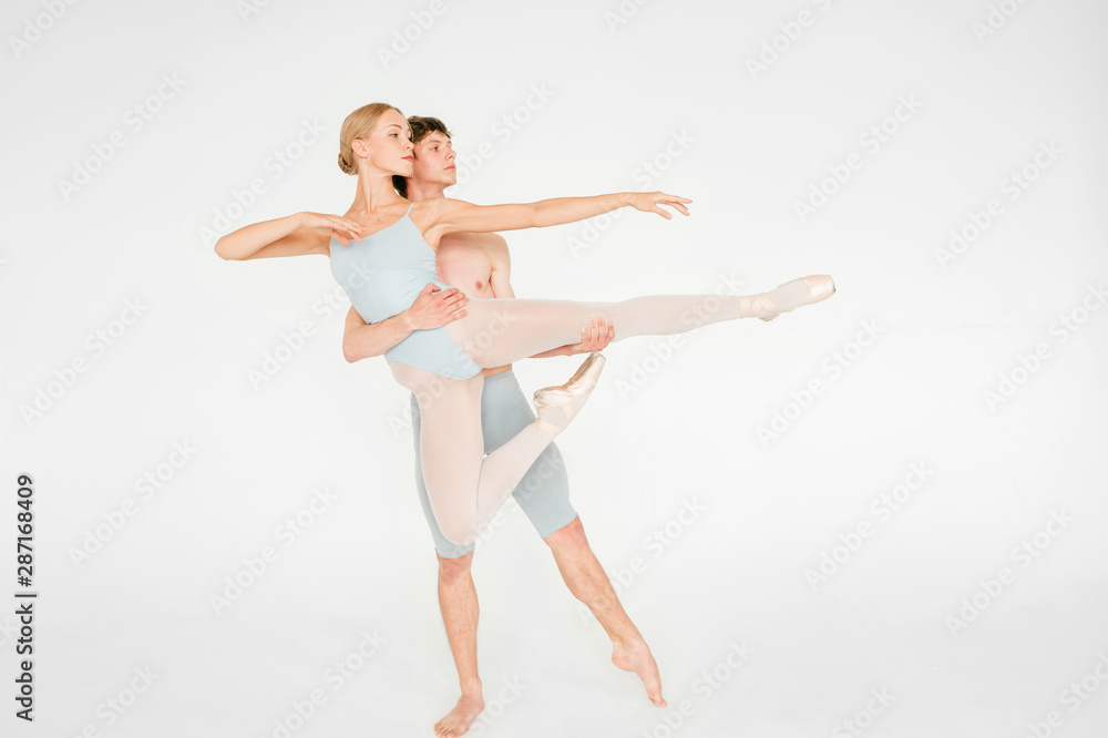 Young couple of modern ballet dancers posing over white studio background